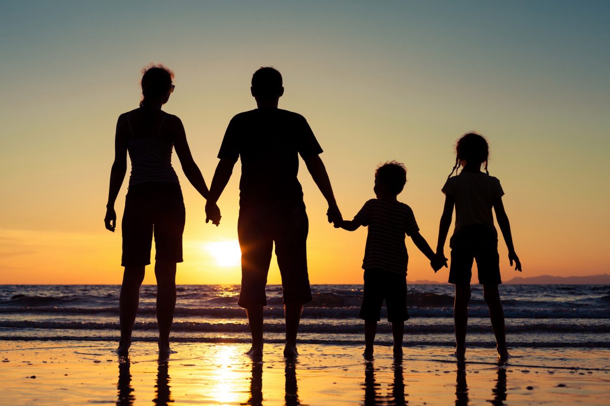 Silhouette of happy family who standing on the beach at the sunset time. Concept of friendly family.